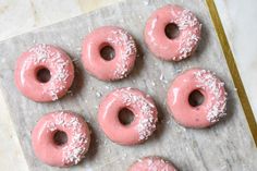 six donuts with pink icing and sprinkles on a baking sheet