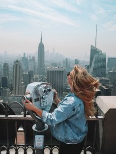 a woman standing on top of a tall building looking at a coin operated machine in front of her