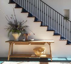 a wooden table sitting under a stair case next to a banister and potted plant