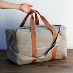 a person holding onto a duffel bag on top of a wooden table