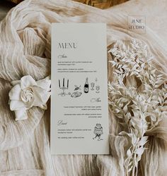 a menu card sitting on top of a bed next to a white flower and napkin