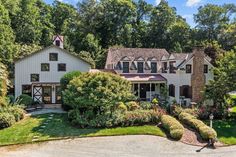 a large white house surrounded by trees and bushes in the middle of a driveway area