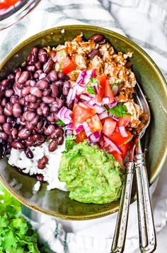 a bowl filled with black beans, guacamole and tomatoes on top of a table