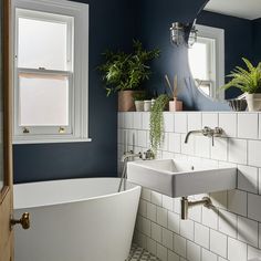 a white bath tub sitting under a bathroom window next to a toilet and sink in a bathroom