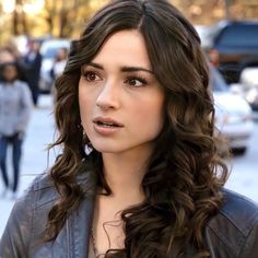 a close up of a person wearing a leather jacket on a street with cars in the background