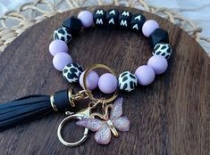 A gorgeous shade of lavender, with black and white cow print silicone beads strung on a doubled-up 5.5m stretch cord up make up this vibrant "Mama" Wristlet Keychain. A gold (alloy metal) split key ring and lobster clasp are attached, along with a black tassel and a resin, iridescent-purple butterfly 🦋 💜 🐄 Cow Print Butterfly, Mama Wristlet, Boho Charms, Black And White Cow Print, White Cow Print, Black And White Cow, 3 Hearts, Print Butterfly, Iridescent Purple