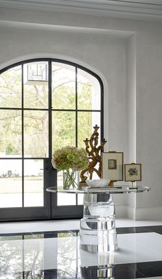 a room with a black and white checkered floor, large arched window, and glass table