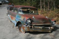 an old rusted out car sitting on the side of a road