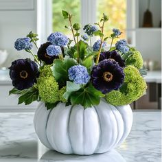 a white pumpkin shaped vase filled with blue and green flowers