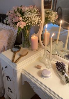 a white dresser topped with a mirror and candles next to a vase filled with flowers