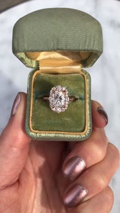 a woman's hand holding an engagement ring in a velvet box with a diamond center