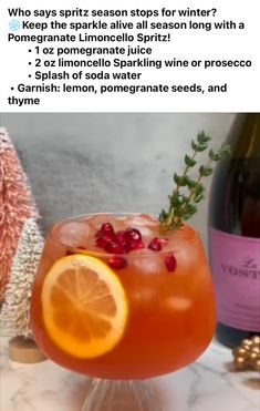 a wine glass filled with an orange and cranberry drink next to a bottle of wine