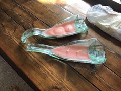 two glass candles sitting on top of a wooden table next to a plastic bag filled with toilet paper