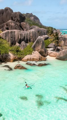 a man riding a surfboard in the ocean next to some rocks and water with green plants