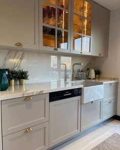 a kitchen with white cabinets and marble counter tops, gold trimmings on the doors