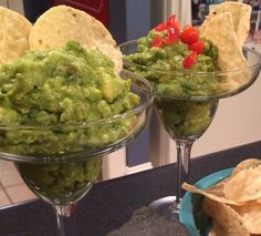 two martini glasses filled with guacamole and tortilla chips on a counter