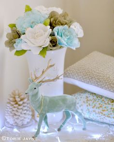 a white vase filled with flowers and a deer figurine sitting next to it