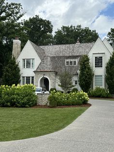 a white house surrounded by lush green trees and shrubbery with a driveway leading to it