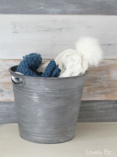 a metal bucket filled with crocheted hats and mittens sitting on top of a table