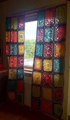 there is a crocheted window curtain in the living room with bright colored squares on it