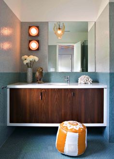 a bathroom with blue and white tiles, an orange stool and a large mirror above the sink