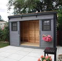 a wooden shed with flowers in the window and on the outside wall, next to a bench