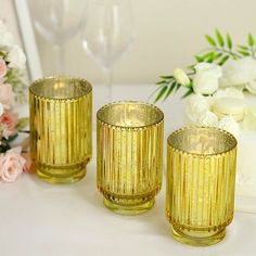 three gold colored glasses sitting on top of a table next to flowers and a cake