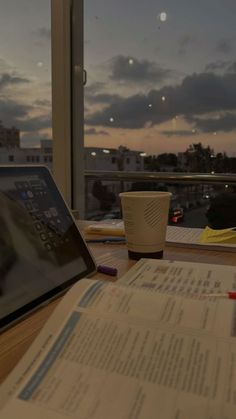 an open laptop computer sitting on top of a wooden desk next to a cup of coffee