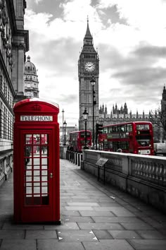 a red phone booth sitting on the side of a road next to a tall clock tower