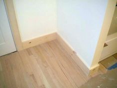 an empty room with white walls and wood flooring in the corner, next to a door