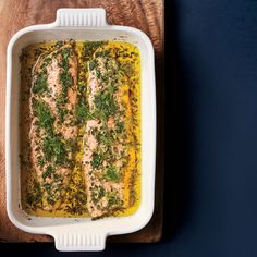 salmon with herbs in a white casserole dish on a wooden cutting board next to a knife