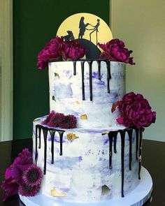 a three tiered cake with purple flowers on the bottom and black icing running down the side