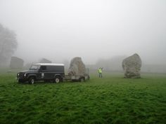 a man standing next to a truck in a field with large rocks on the side