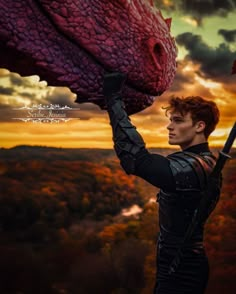 a young man holding up a large dragon statue in front of a sunset sky with clouds