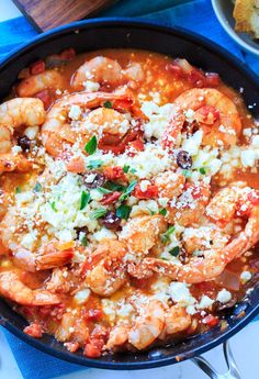 a skillet filled with shrimp and cheese on top of a blue cloth next to bread