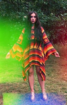 a woman with long hair standing in the grass wearing a multicolored dress and white shoes