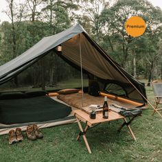 a tent set up in the middle of a field with two chairs and a table next to it