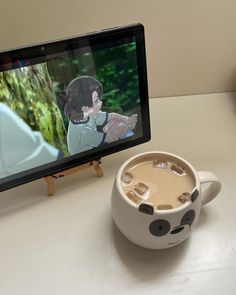 a cup of coffee sitting next to a tablet computer on a table with an animated screen in the background