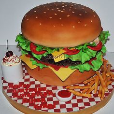 a large hamburger with lettuce, tomatoes and cheese next to fries on a checkered table cloth