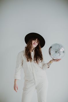 a woman in white jumpsuits and a black hat holding a silver disco ball