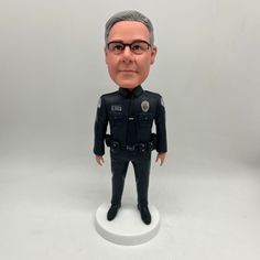 a custom bobble head police officer on a white base with grey hair and glasses