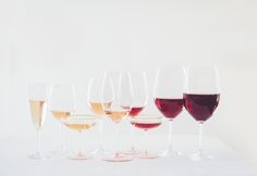 several glasses of wine lined up in a row on a white table top with one glass half full and the other half empty