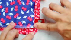 two hands are working on a piece of fabric that has cherries printed on it