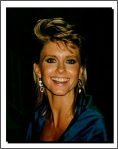 a woman in a blue dress smiling at the camera with big earrings on her head