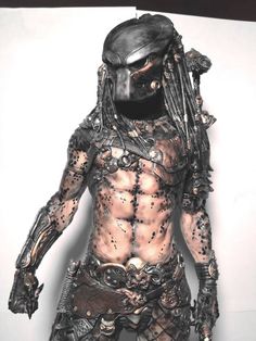 a man dressed up as predator with metal armor and headgear, standing in front of a white wall