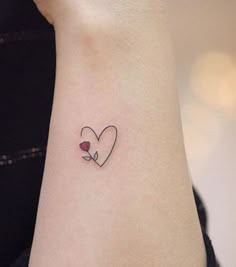 a small tattoo on the wrist of a woman with a heart and flower in it