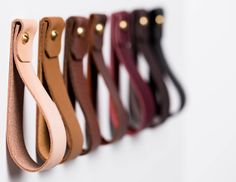 a row of different colored leather handles hanging on a wall