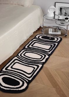 a white bed sitting next to a black and white rug on top of a wooden floor