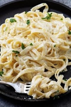 a black plate filled with pasta and parsley on top of a gray tablecloth