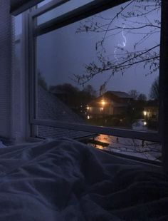 a bedroom with a window that has snow on the ground and trees outside at night